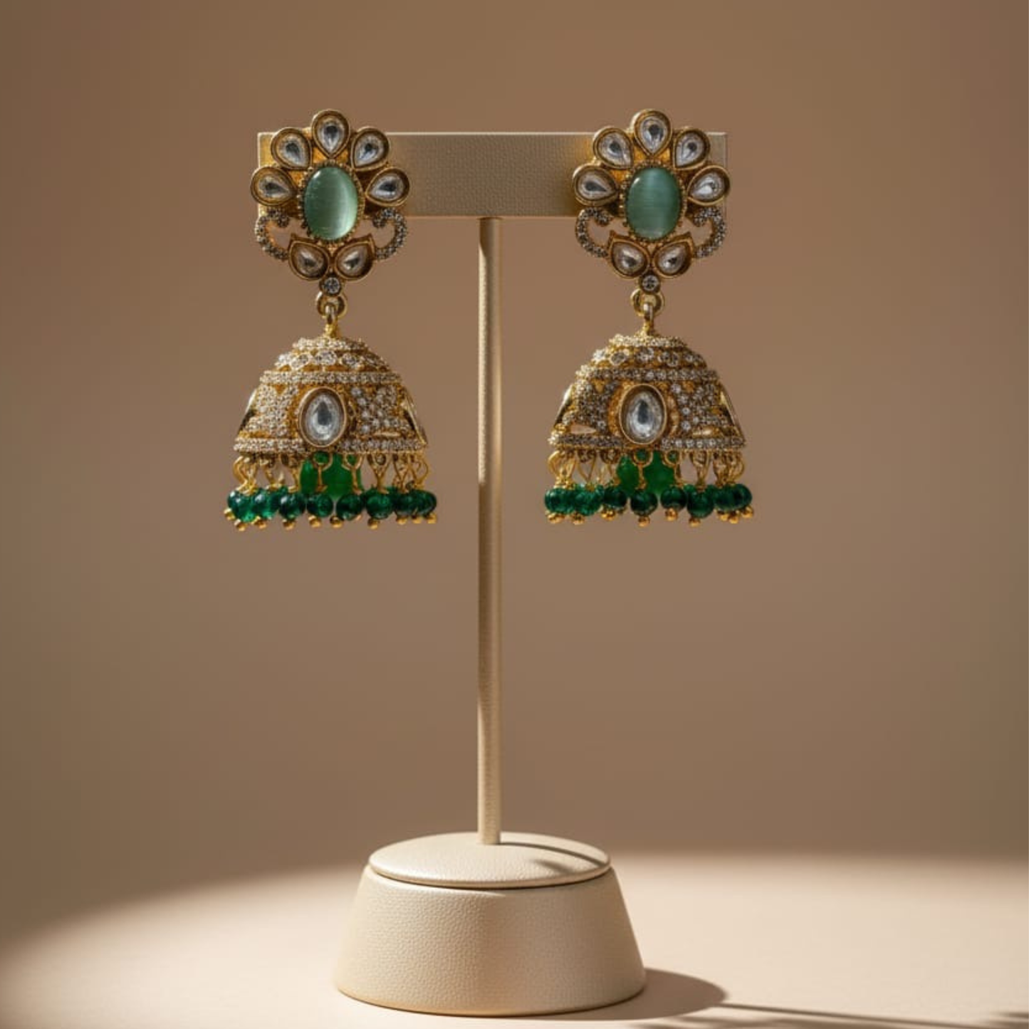 Gold earrings with green stones and kundan detailing on maroon fabric background