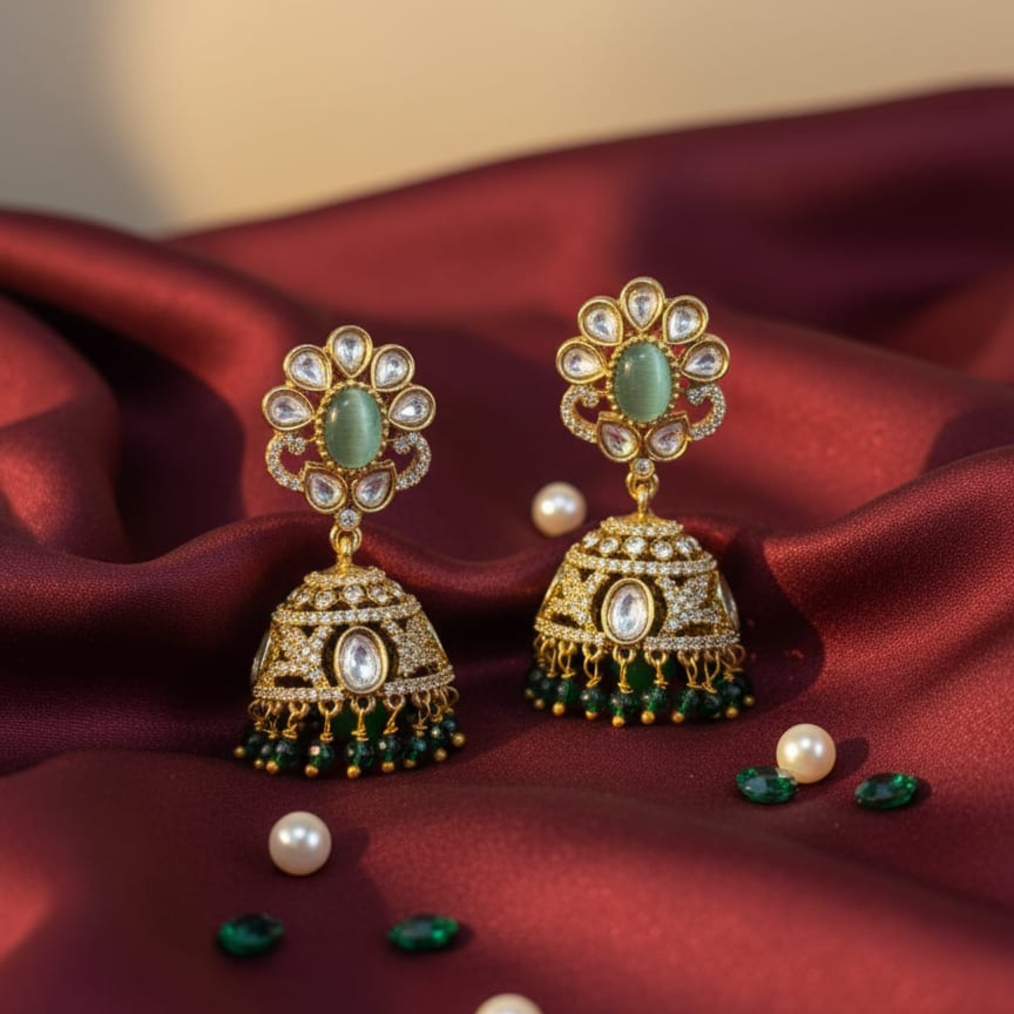 Gold earrings with green stones and kundan detailing on maroon fabric background